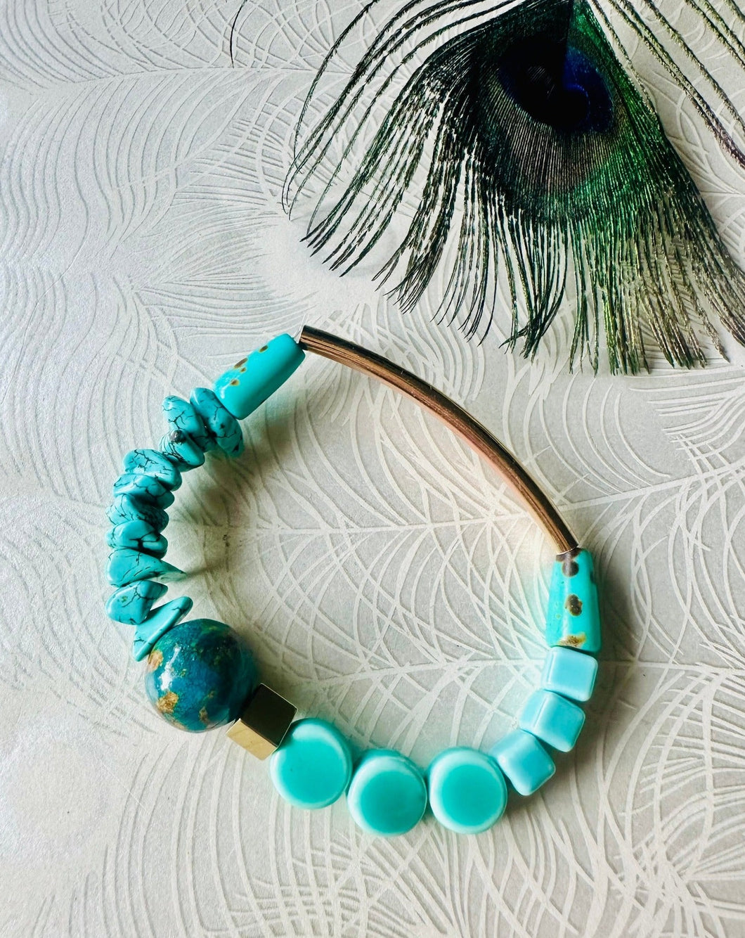 gemstone turquoise ceramic & gold hematite bead bracelet on a white peacock feather background