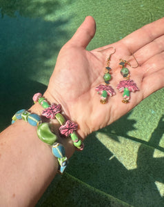 Pink &amp; green ceramic palm tree earrings with matching bracelets on wrist over pool