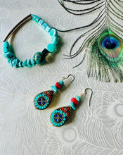 Load image into Gallery viewer, gemstone turquoise ceramic &amp; gold hematite bead bracelet on a white peacock feather background next to a matching pair of turquoise &amp; red earrings