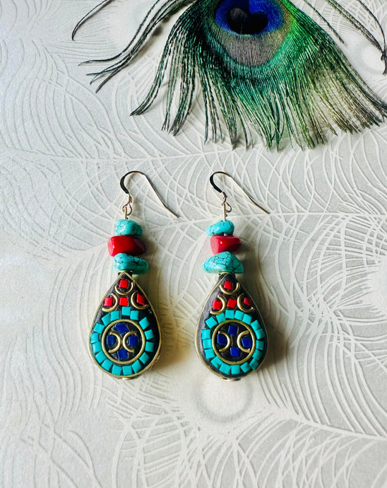 Turquoise gemstone & red coral earrings with black & gold teardrop feature bead & 14ct gold filled ear hooks on a peacock paper background with a peacock feather above