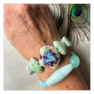 Pale green ceramic bracelet with ceramic shell feature bead &amp; assorted shaped ceramic beads on freckled arm with peacock feather 