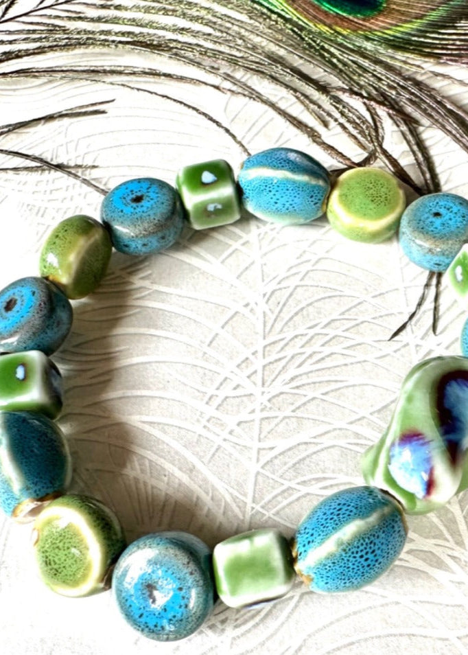 Turquoise & green ceramic multishaped beaded bracelet  on stretch elastic on a peacock paper background with a real peacock feather above