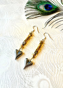 Silver heart earrings with gold and hematite beads next to a peacock feather 
