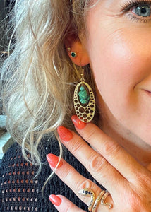 gold oval earrings with turquoise stone pieces worn by blue  eyed blond haired girl with black top & gold snake ring on her hand