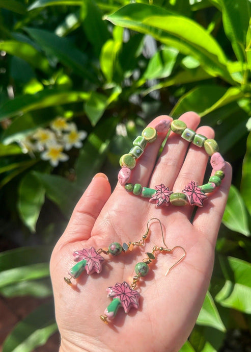 Pink & green ceramic palm tree earrings with matching bracelet on hand with frangipani tree behind