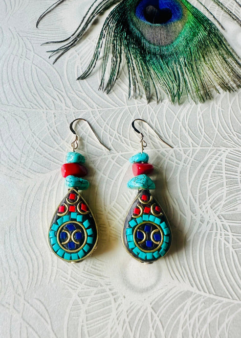 Turquoise gemstone & red coral earrings with black & gold teardrop feature bead & 14ct gold filled ear hooks on a peacock paper background with a peacock feather above