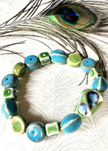 Load image into Gallery viewer, Turquoise &amp; green ceramic multishaped beaded bracelet&nbsp; on stretch elastic on a peacock paper background with a real peacock feather above