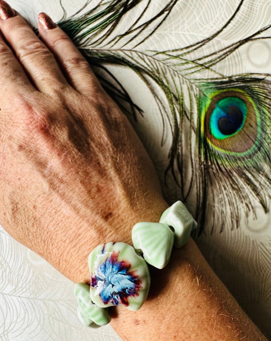 Pale green ceramic bracelet with ceramic shell feature bead & assorted shaped ceramic beads on freckled arm with peacock feather 