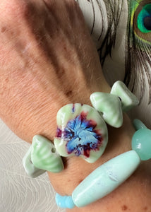 Pale green ceramic bracelet with ceramic shell feature bead &amp; assorted shaped ceramic beads on freckled arm with peacock feather 