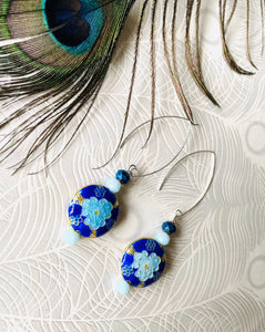 Iridescent Cobalt blue round enamel cloissone flower design earrings including Swarovski crystal & sterling silver textured long ear hooks sitting on white background with peacock feather