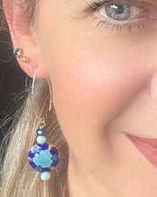 Load image into Gallery viewer, Iridescent Cobalt blue round enamel cloissone flower design earrings including Swarovski crystal &amp; sterling silver textured long ear hooks worn on the ear of a blonde haired model with blue eye