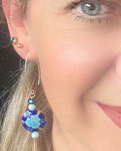 Iridescent Cobalt blue round enamel cloissone flower design earrings including Swarovski crystal & sterling silver textured long ear hooks worn on the ear of a blonde haired model with blue eye