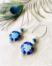 Load image into Gallery viewer, Iridescent Cobalt blue round enamel cloissone flower design earrings including Swarovski crystal &amp; sterling silver textured long ear hooks sitting on white background with peacock feather