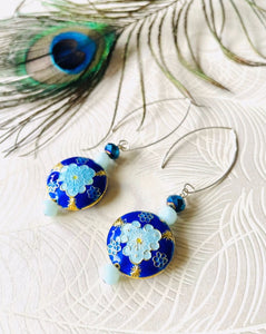 Iridescent Cobalt blue round enamel cloissone flower design earrings including Swarovski crystal & sterling silver textured long ear hooks sitting on white background with peacock feather