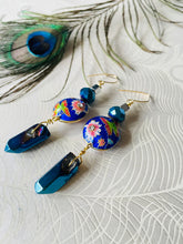 Load image into Gallery viewer, Iridescent Cobalt blue raw quartz pointed stone earrings with round enamel flower &amp; butterfly design, including Swarovski crystal &amp; 14ct gold filled ear hooks sitting on a white background with a peacock feather