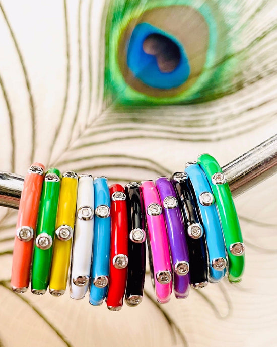 A range of coloured enamel stacking rings  on a silver bar with peacock feather background