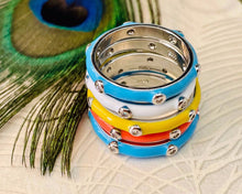 Load image into Gallery viewer, Blue, orange, yellow and white enamel stacking rings piled up with a peacock feather next to them