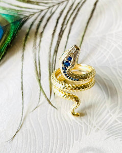 gold engraved coiled snake ring with blue and clear CZ stones against a white background with peacock feather