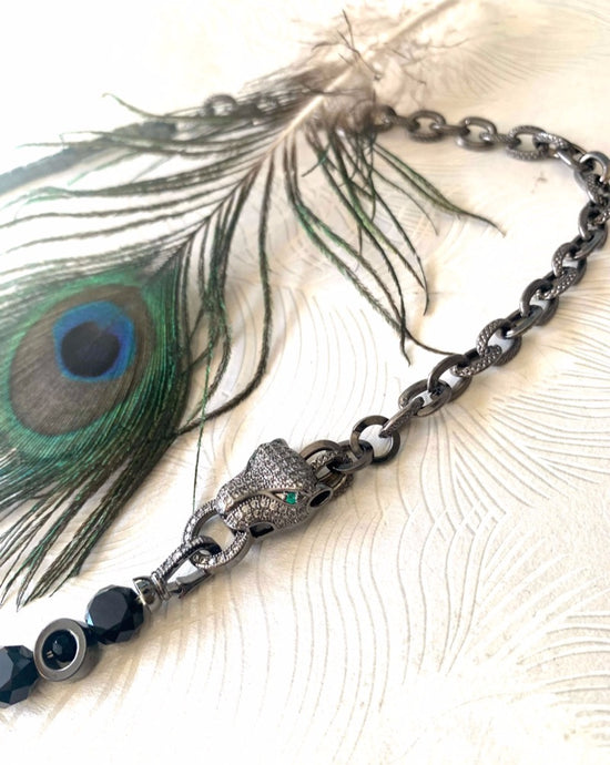 close up of a Black toned pave' crystal embellished panther with green crystal eyes. Hematite Stone beads & Czech crystal beaded necklace with gunmetal chain next to a peacock feather