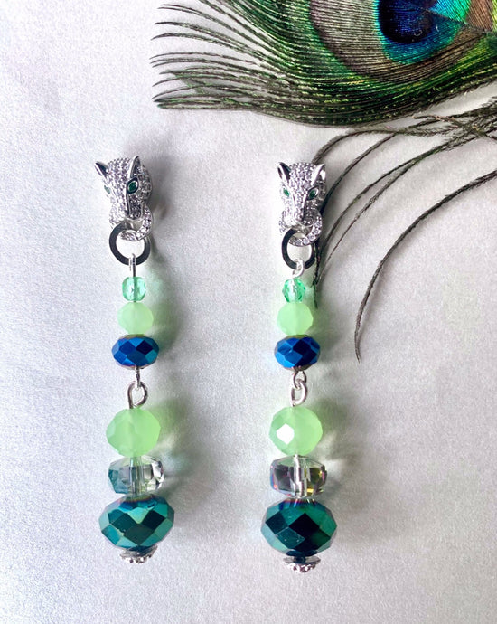 Czech crystal beads hanging from silver toned pave panther studs with green crystal eyes. Stud back earrings on white background with peacock feather