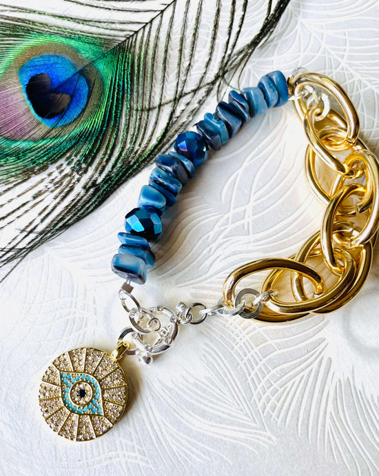Silver crystal embellished Toggle fastening bracelet with mix of silver & gold toned chain with Bright blue Crystal & shell beads & an 18ct gold plated crystal encrusted evil eye pendant with peacock feather