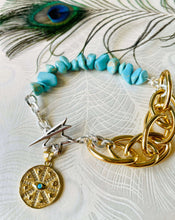 Load image into Gallery viewer, Sterling Silver Star shaped toggle fastening bracelet with mix of silver &amp; gold toned handmade chain with turquoise beads &amp; an 18ct gold plated crystal encrusted turquoise evil eye charm plated in 18ct gold on peacock featherpatterned paper with feather in background