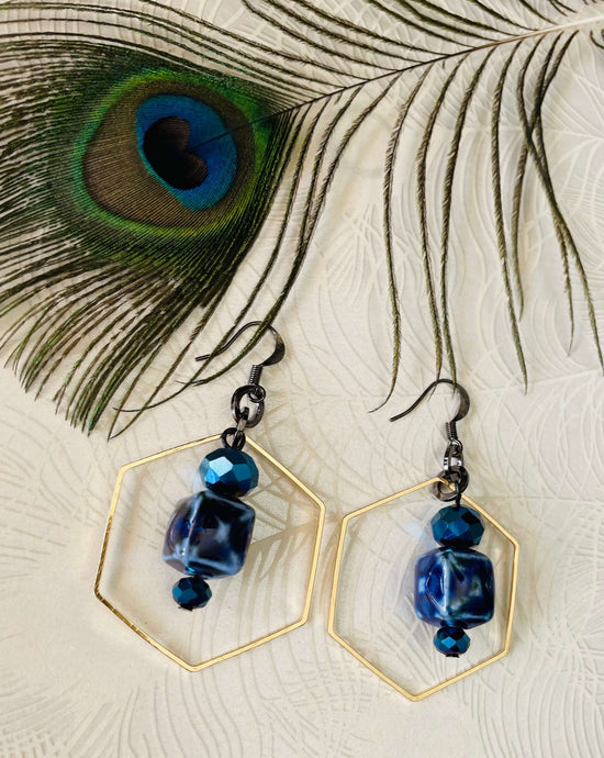 Cobalt blue ceramic & bright blue crystal earrings with brass hexagon feature & gunmetal links and hooks on peacockpatwerned background with peacock feather