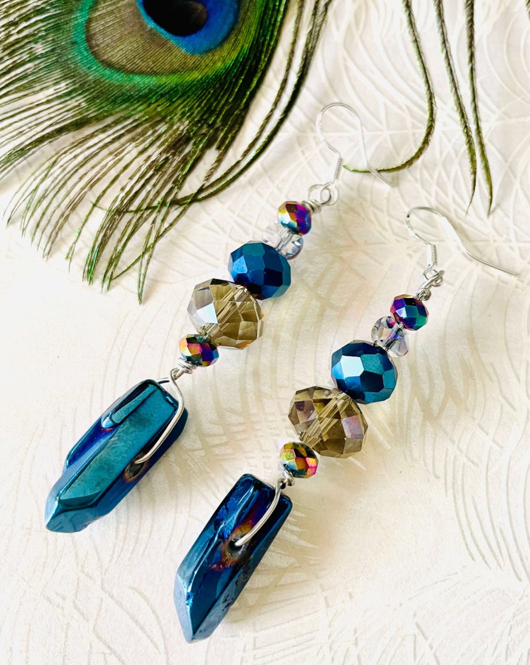 Iridescent blue raw quartz pointed stone earrings with Smokey quartz brown toned Swarovski crystal & sterling silver ear hooks on peacock feather patterned background