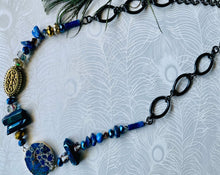 Load image into Gallery viewer, Bright cobalt Blue Lapis Lazuli gemstone and gold hematite with crystal statement necklace sitting on a white background next to a peacock feather
