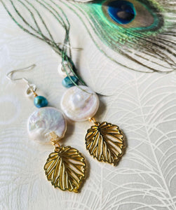 gold-leaf-charm-with-white-20mm-keshi-coin-pearl-turquoisr freshwater -pearl-hanging-from-silver-ear-hook-next-to-peacock-feather