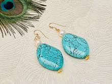 Load image into Gallery viewer, Large turquoise oval gemstone earring with small freshwater white pearl and gold ear hooks against a white background with a peacock feather
