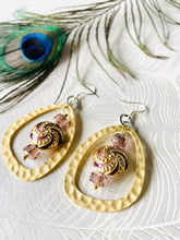 Load image into Gallery viewer, Purple &amp; Gold round enamel Cloisonné Bead earrings including gold plated hammered finish loop with crystals &amp; sterling silver ear hooks sitting on paper with a peacock feather in the background