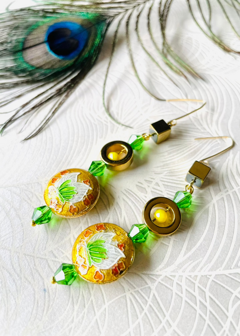 Green & yellow round enamel cloissone flower design earrings including gold hematite & Swarovski crystals & 14ct gold filled ear hooks on white background with peacock feather