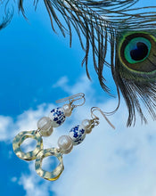 Load image into Gallery viewer, Blue &amp; white flower ceramic bead earrings with Genuine Freshwater Pearls Gold Plated textured feature discs with 14Ct Gold Filled ﻿ear hooks sitting on a background of blue sky with clouds and a peacock feather