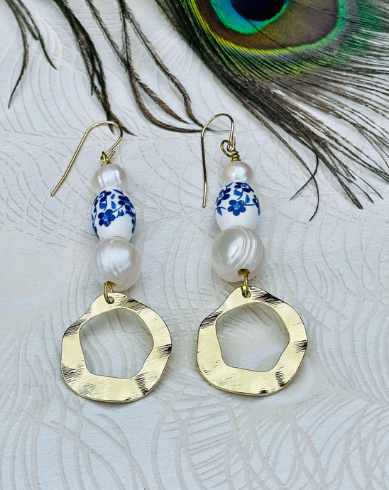 Blue & white flower ceramic bead earrings with Genuine Freshwater Pearls Gold Plated textured feature discs with 14Ct Gold Filled ﻿ear hooks sitting on a background of patterned paper and a peacock feather  Edit alt text