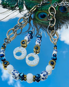 Necklace with blue & white ceramic flower beads, gold hematite  & cobalt blue & white Czech crystal beads with a silver clasp with gold & silver toned chain on a sky background with peacock feathers & matching earrings
