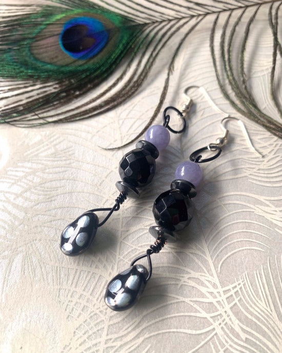 Black Czech glass with silver polka dot, black Czech crystal & lavender quartz with sterling silver ear hooks  on peacock patterened paper with a peacock feather in the background