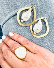 Load image into Gallery viewer, Gold restatement ring with mother of pearl inlay  worn on a hand against a pair of blue jeans with a pair of gold &amp; white enamel leaf earrings