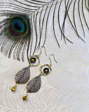 Load image into Gallery viewer, Silver metal leaf earrings with black Hematite, gold crystal &amp; metal twisted loops on sterling silver ear hooks. sitting on peacock patterned paper with peacock feather in top left corner
