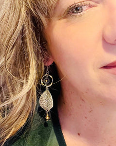 Silver metal leaf earrings with black Hematite, gold crystal & metal twisted loops on sterling silver ear hooks. on a blonde haired model with green shirt