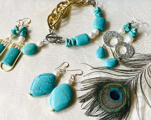 Turquoise large stone bracelet with keshi pearls and mixed gold chunky chain with silver clasp & turquoise and pearl charm with 3 pairs of matching turquoise gold & silver earrings on a cream background with a peacock feather