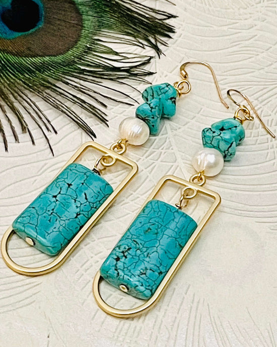 Turquoise pillow shape stone with gold frame  freshwater pearl and turquoise earring against a light background with a peacock feather