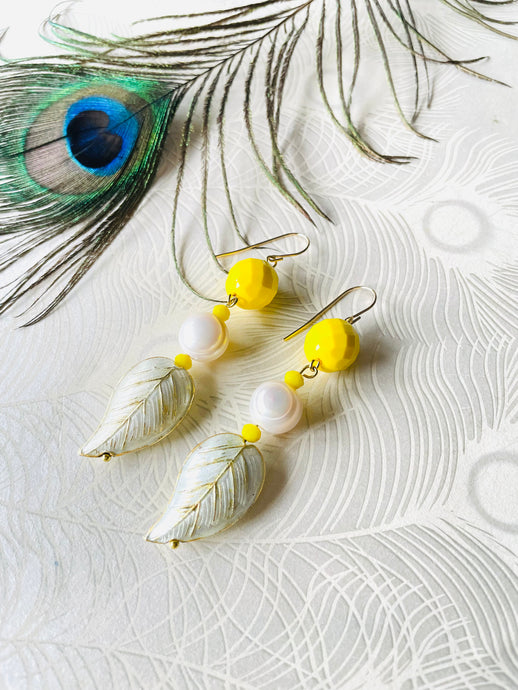 white & gold leaf shaped cloissonne earring with pearls & yellow faceted crystal beads on a gold ear hook sitting on a white background with a peacock feather